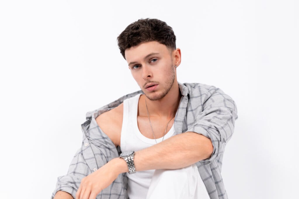 Exclusive Interview: Scott the Pisces chats about his new music, his latest release "Euphoric" featuring Ashley Alisha, and his career to date 74 Scott the Pisces posing for a photoshoot, wearing a white vest top over an open grey shirt. He has one arm on his knee.