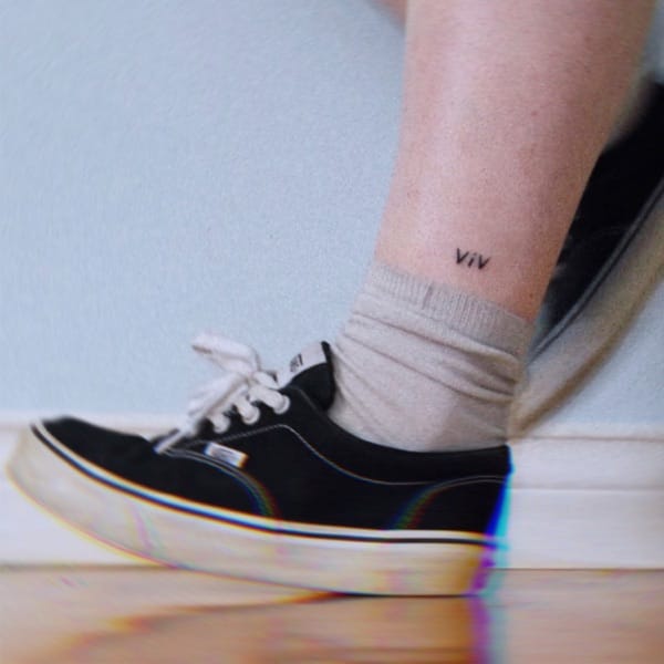 Single cover artwork for "Viv" by Ash Molloy which sees a Vans trainer on a hardwood floor, against a white wall, with a grey sock, with a tattoo of the name "Viv" against white skin. We presume this is Ash Molloy's leg.