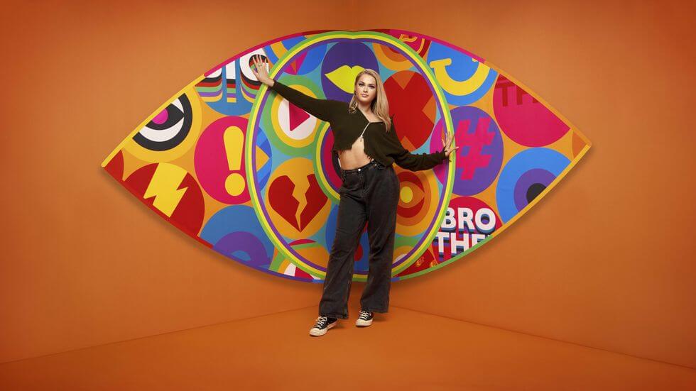 Big Brother UK 2023 Makes a Grand Comeback with Exciting New Housemates and Punishing Games 151 Big Brother 2023 housemate Hallie standing in front of the new eye logo with a bright orange background.