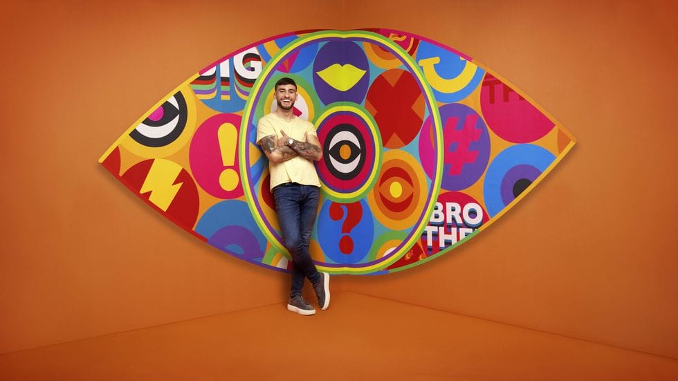 Big Brother UK 2023 Makes a Grand Comeback with Exciting New Housemates and Punishing Games 160 Big Brother 2023 housemate Paul standing in front of the new eye logo with a bright orange background.