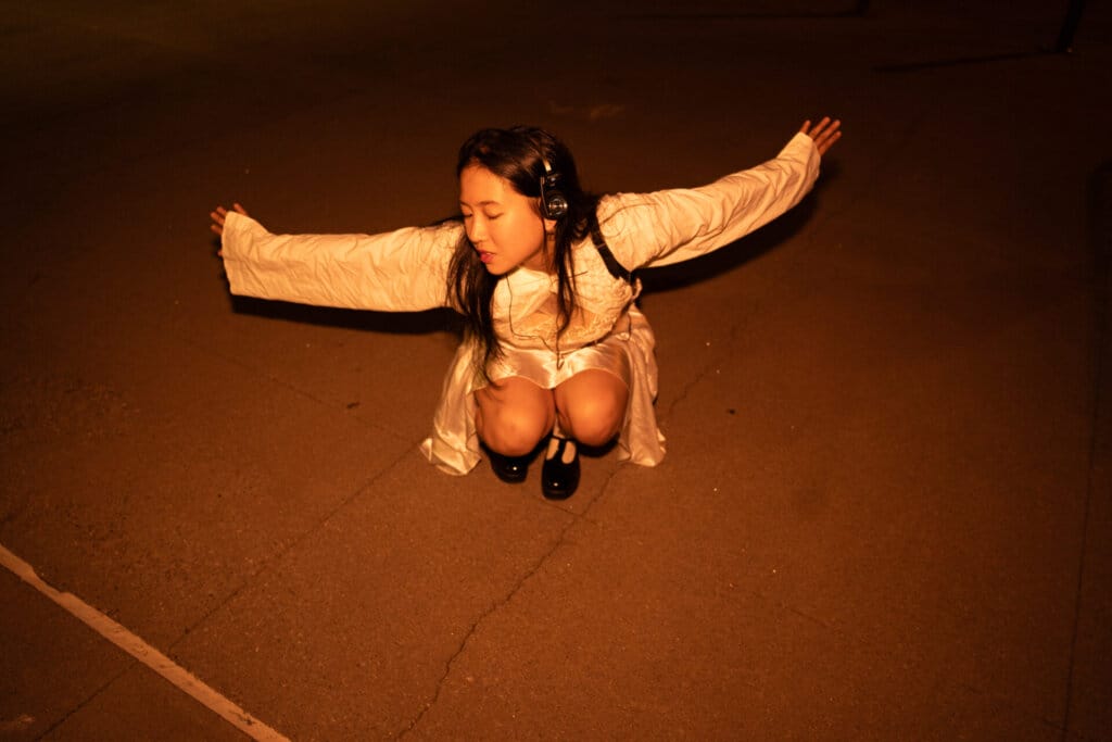 ÊMIA Unveils Sensational Sequel EP "VIDEO CALL: PM" - A Captivating Musical Journey of Emotions and Connection 68 Promotional image for "VIDEO CALL: PM" which sees ÊMIA posing by crouching down in a white top and a cream silk dress as she flings her arms open for the photo.