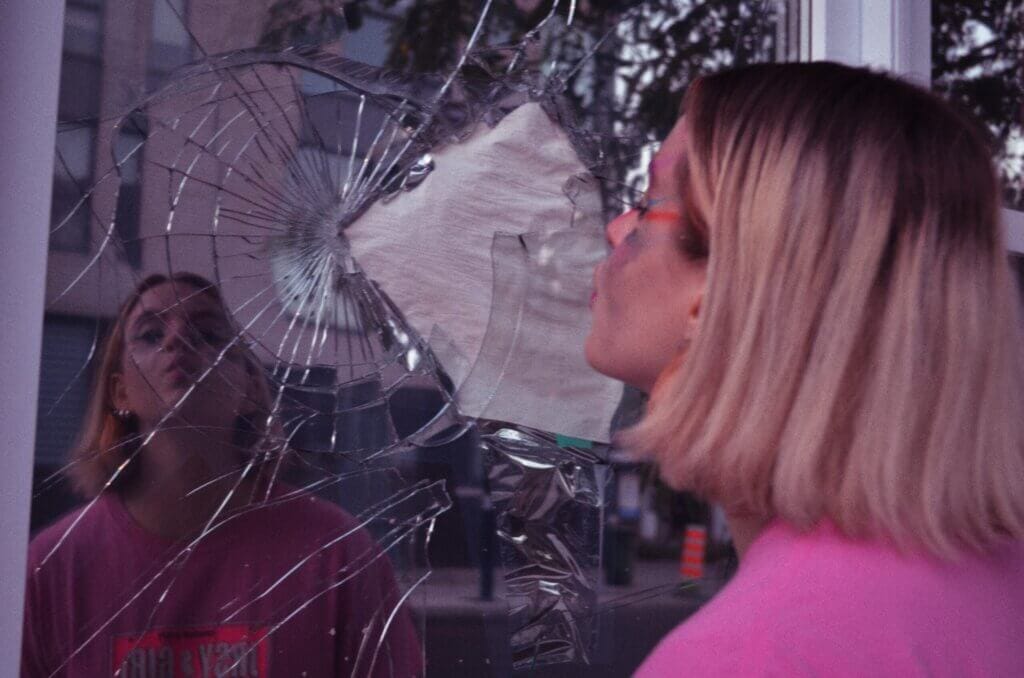 Malade looking in a broken mirrored glass on a building for a promotional photo for "Give Up".