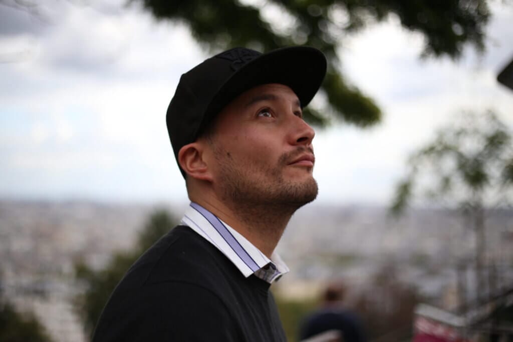 Promotional image for "Red Planet" which sees a head shot of Alex Maher facing the right as he wears a black sweater and a black cap with a countryside landscape blurred in the background.