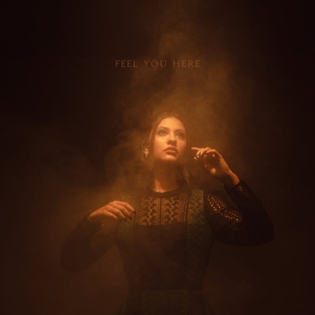 "Feel You Here": Alaina Pamela Takes Viewers on an Emotional Journey with New Music Video 14 Official single artwork for "Feel You Here" which sees Alaina Pamela lightly illumed amongst smoke, wearing a long-sleeved black dress.