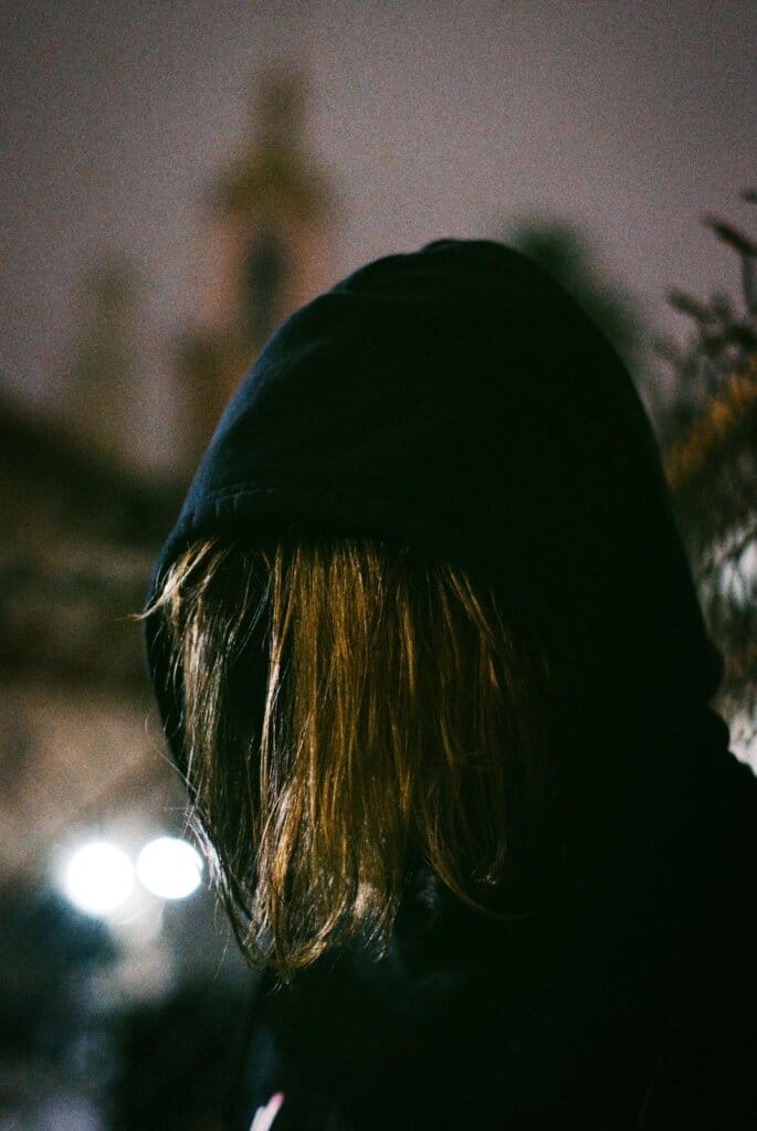 Promotional head shot photo of Sam Kallan with the hood of his black hoodie up over his head and his long dirty-blonde hair covering his face.