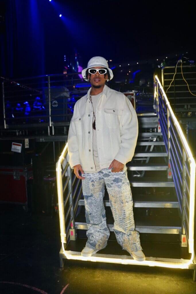 Yung Wylin: Crafting Impressive Musical Euphoria with "Good Energy" 6 Promotional image of Yung Wylin for "Good Energy" which sees him backstage on the stairs to the stage, posing in a white denim jacket, blue ripped jeans, white trainers, a white hat and white-rimmed shades.