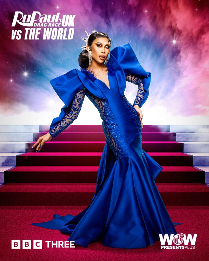 Slaying the World: Follow the Queens of RuPaul's Drag Race UK vs the World Series 2 105 Marina Summers from RuPaul's Drag Race UK vs the World series 2, posing in a blue silk dress with a red carpet of stairs behind her.