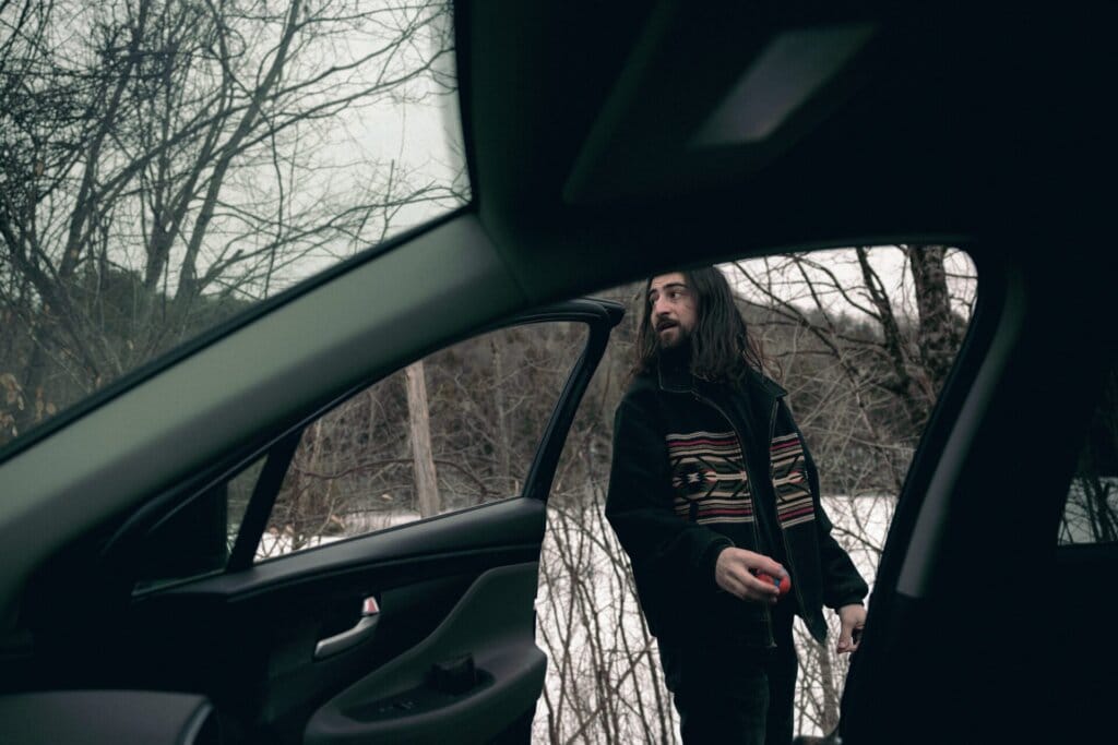 The Season of Noah Kahan: Vermont Singer-Songwriter Celebrates the Official Chart Double With "Stick Season" 34 Promotional photo for "Stick Season" which sees the current Chart Double artist, Noah Kahan looking over his shoulder as he is outside a car, while the camera is inside the car.