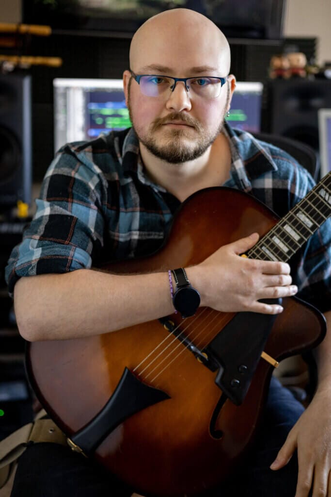 "Jump In": Shaun Chasin Unveils Mesmerisingly Memorable Music Video with Eclectic Influences 2 Promotional photo for "Jump In" which sees Shaun Chasin holding a guitar close to his chest, in the studio, with the producing decks behind him.