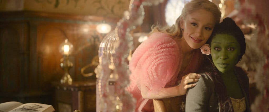 Prepare to Defy Gravity With the Witches of Oz: Wicked Film Trailer Soars with Spectacular Visuals and Unforgettable Performances 19 Glinda looking over Elphaba's shoulder as they both look in the mirror.