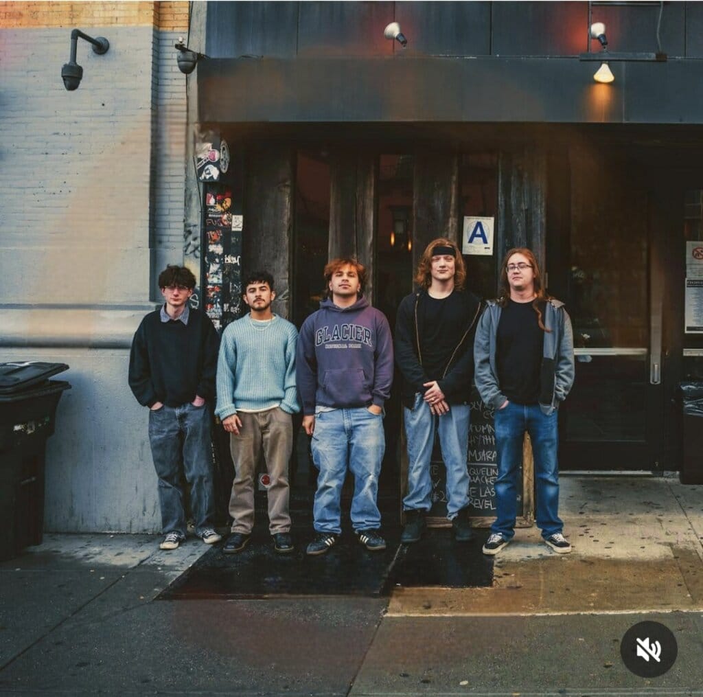 SAMSARA. posing in jeans and hoodies out on a street outside a wooden-beamed store.