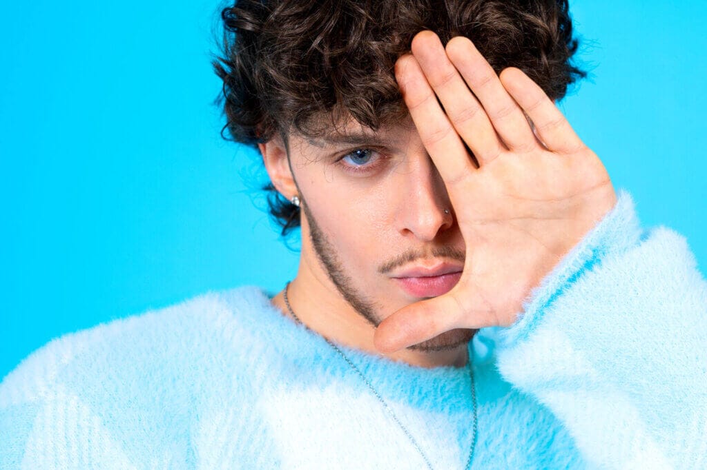 "Delusional": Scott the Pisces Brings the Heat for His Awesome New Summer Smash Single Featuring Mimi Sky 23 Promotional photo for "Delusional" which sees a headshot of Scott the Pisces in the photo studio, wearing a baby blue jumper with one hand up against his face with his palm out to the camera.