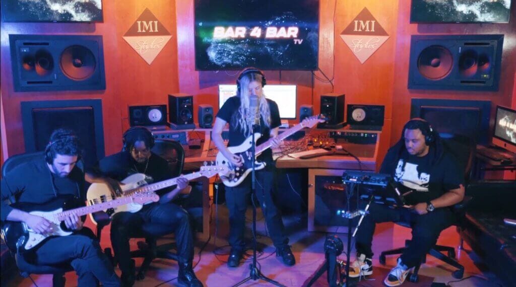 Madison Arruda Releases Dreamy New Single “Let Me In” Alongside Live Performance Video 3 Madison Arruda performing "Let Me In" at the IMI Studios with two guitarists to her right and a drummer to her left while she's wearing black and standing in front of a microphone, holding a guitar.