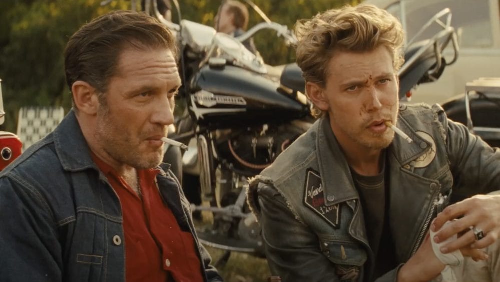 The Bikeriders Film Review: Jodie Comer Commands the Screen Through A Journey of Rebellion and Loyalty 10 Tom Hardy and Austin Butler as Johnny and Billy, sitting on some grass in front of their motorcycles.