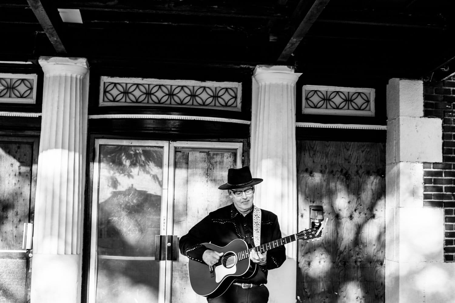 "Carolina": The FrannyO Show’s New Single Explores the Meaning of Home 3 Black and white photo of Fran O'Connell performing as The FrannyO Show on the streets, outside a store, with a guitar around him and a hat. It looks like he's busking.