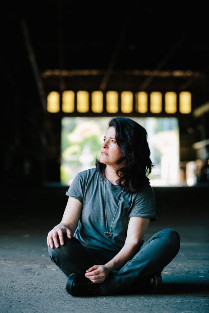 "Cry With Me": Experience the Emotional Depth of Stephanie Schneiderman's New Single 5 Stephanie Schneidman posing in the Zidell Shipyards wearing a loose-fitted grey t-shirt sitting on the floor looking to the left.