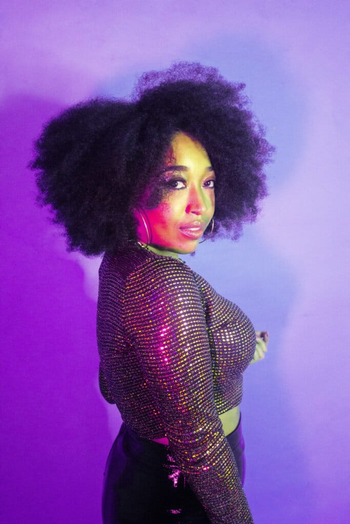 NYC Web Fest Returns to The Producers Club for its 11th Edition and Announces Full Jury Line-Up 52 Professional photo of Cylla Senii, posing in front of a purple background, looking over one shoulder at the camera and wearing a deep purple outfit.