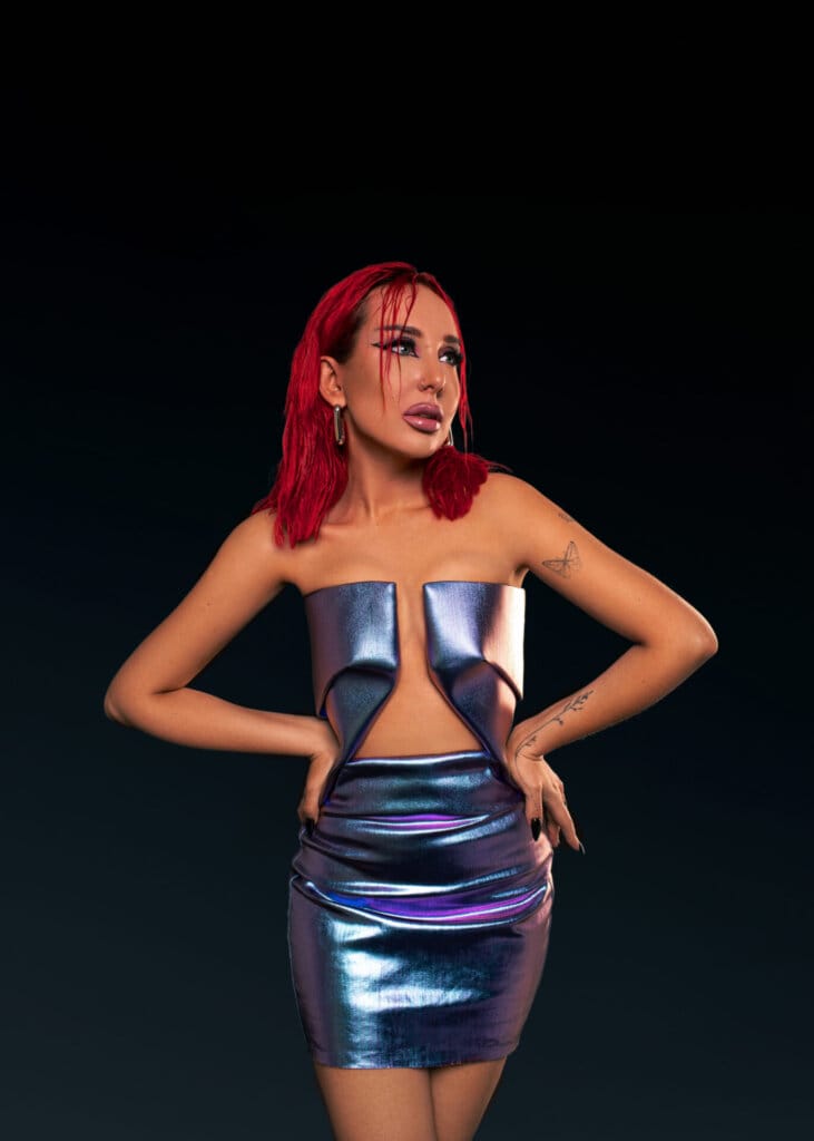 "Stillness": Ukrainian Vocal DJ SHADU's Powerful New EP in the Afrohouse Scene 2 A portrait professional photo of SHADU posing in promotion of "Stillness" where she has her hands on her hips, with a metallic skirt and top which contrasts well with her bright red hair.