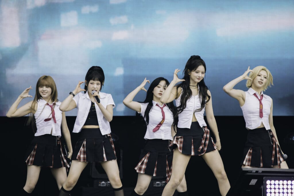 All six band members of the girl group NMIXX performing on the Great Oak Stage at BST Hyde Park wearing school-girl outfits.