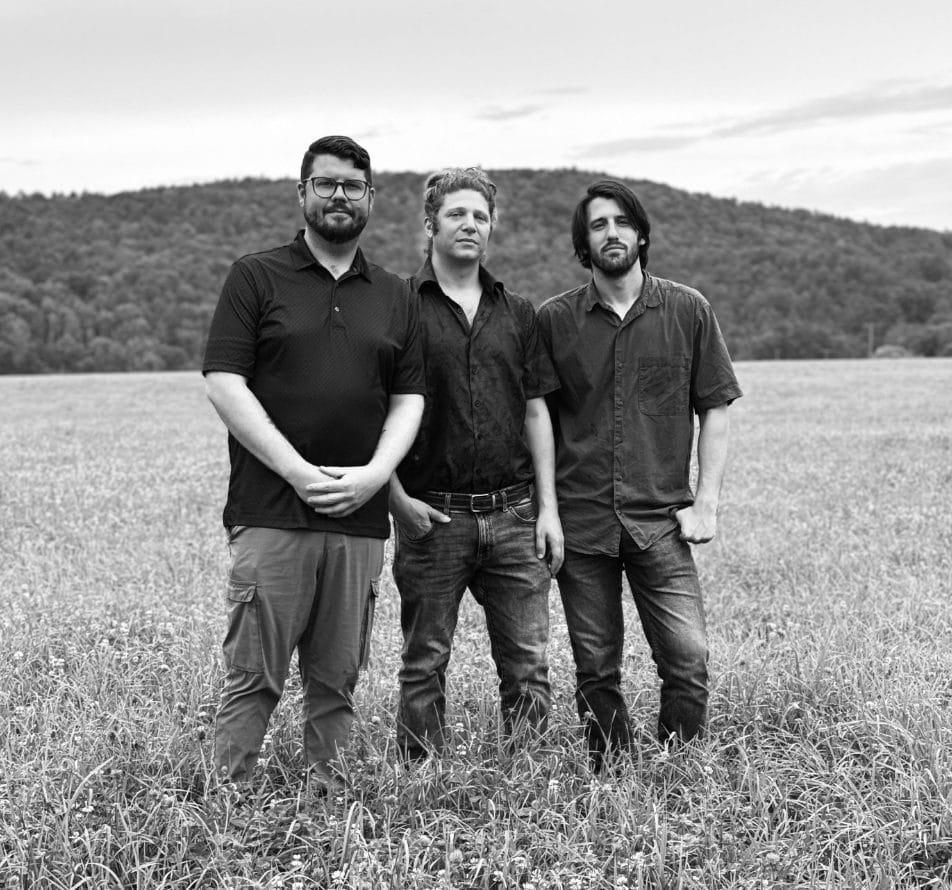 Black and white promotional photo which shows FAR Trio standing together in a field.