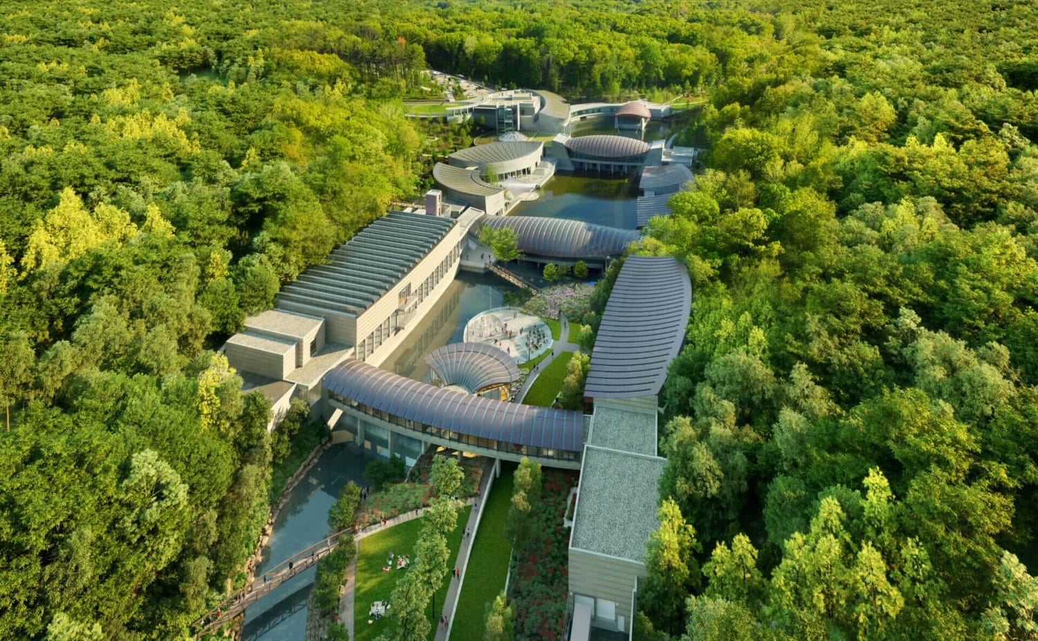 Crystal Bridges Museum Announces KAWS: FAMILY Exhibition for 2025 4 The Crystal Bridges museum which looks like a combination of similar buildings that are nestled amongst a forest and is built just above a lot of water looking like a river.