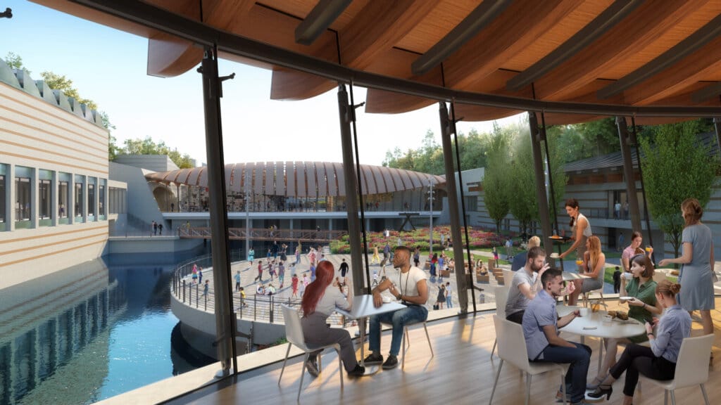 Crystal Bridges Museum Announces KAWS: FAMILY Exhibition for 2025 7 A few people sitting around tables in a cafe area with floor-to-ceiling windows that overlook the water and the museum gallery buildings.