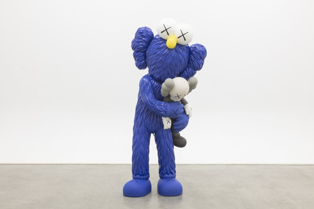 Crystal Bridges Museum Announces KAWS: FAMILY Exhibition for 2025 8 Image of KAWS: TAKE which shows a blue figure holding tightly to a plushie of a similar figure in monochrome greyscale.