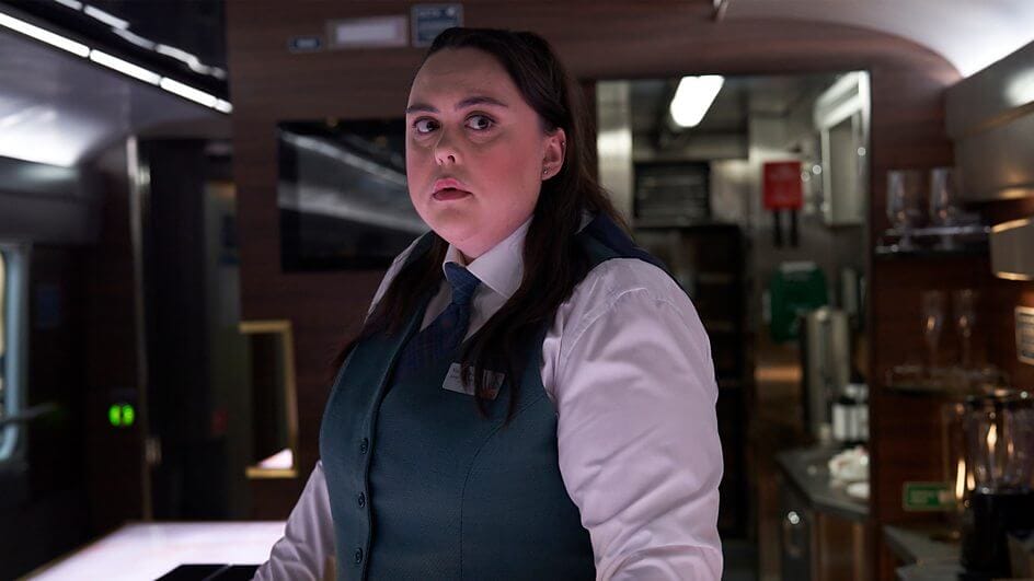 A still from the Nightsleeper trailer which sees Sharon Rooney dressed in a train worker's uniform, looking down the train carriage.