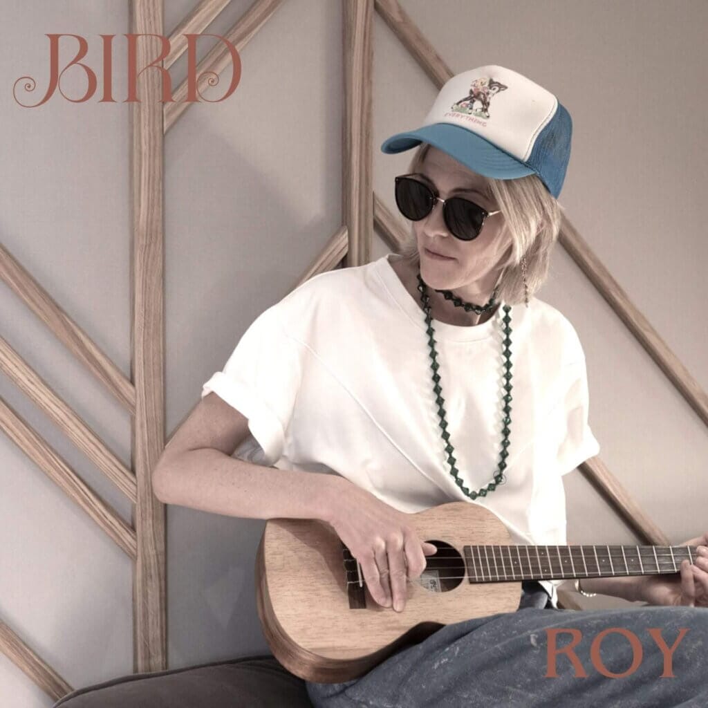 Official single cover artwork for "Roy" which sees Bird sitting down outside and playing a guitar while wearing a white t-shirt accompanied by a pair of sunglasses, a blue-and-white baseball cap, and a black necklace.