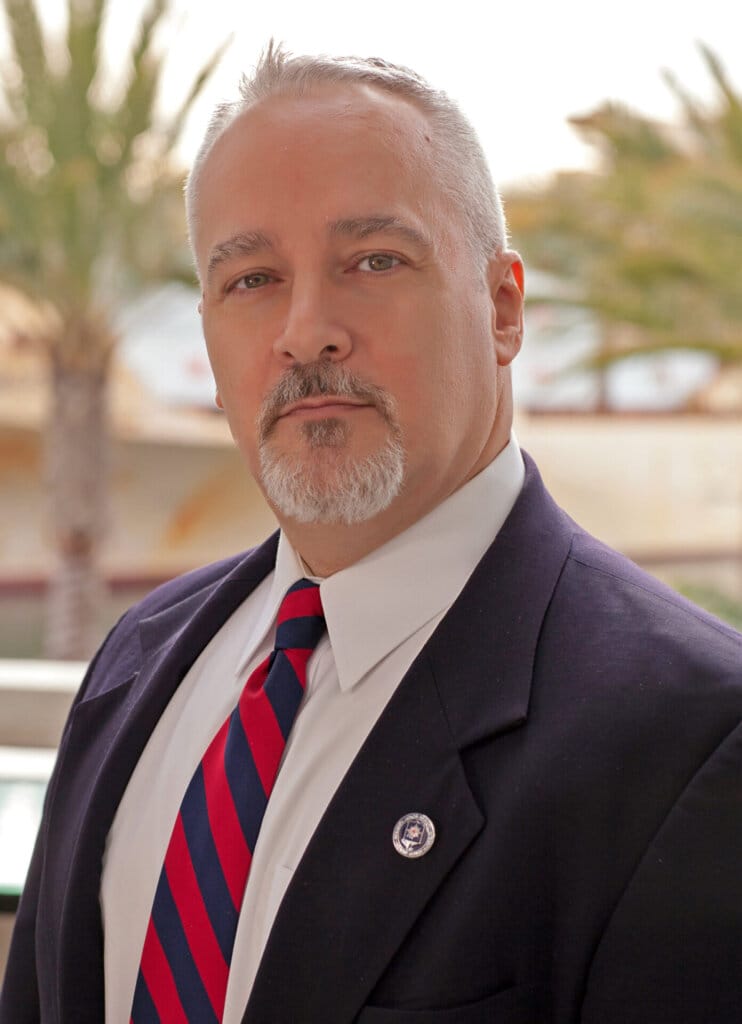 Headshot of Robert Marro Jr. who is wearing a suit with a red and blue-striped tie.