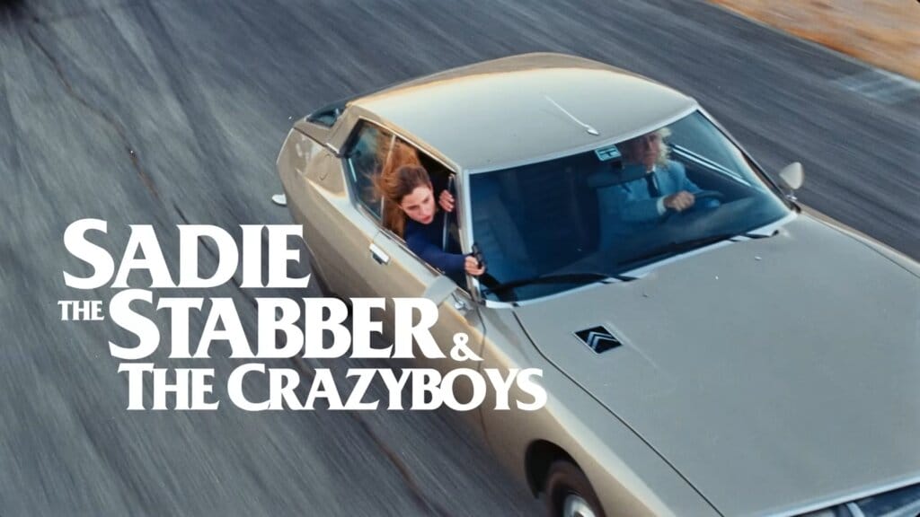 Still from the "Joyride" music video which sees Anna Malygon starring as Sadie the Stabber and the Crazyboys, firing at Kesha out the window of her car, failing to hit her.