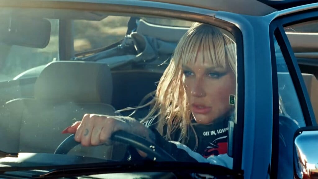 Still from the "Joyride" music video which sees Kesha driving a car with her hands on the steering wheel.