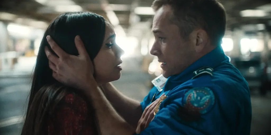Netflix's Carry-On Epic Film Trailer: Sofia Carson and Taron Egerton Heat Up a Romance That Jason Bateman Turns Into a Suspenseful Thriller 46 Still from Netflix's Carry-On film trailer which shows Taron Egerton and Sofia Carson in a carpark, facing one another with Egerton's hands on either side of Carson's head, both looking scared.