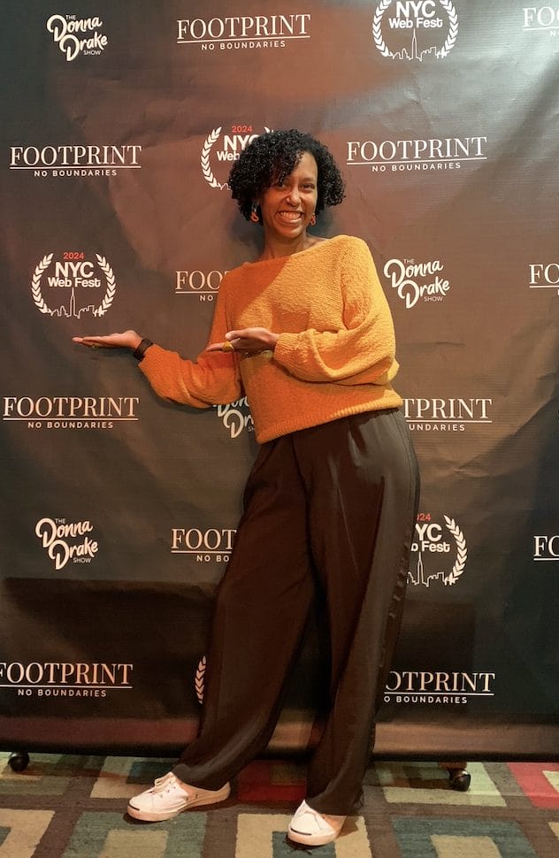 MelimeL posing in front of the NYC Web Fest logo banner which also has Donna Drake and Footprint Network logos on.