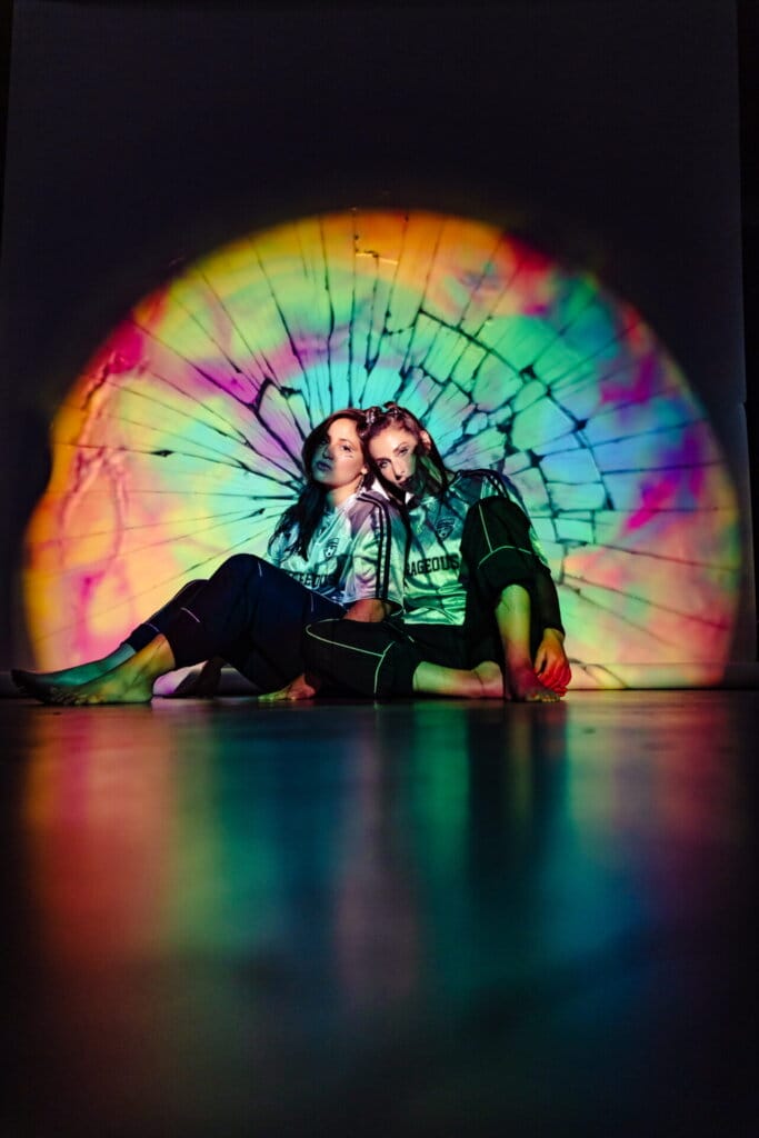 Royal She Reflects on New Single "Karma", Their Rising Success, and Forthcoming Debut Album "Befores and Afters" in Our Exclusive Interview 69 Royal She posing together on the floor with their backs to a wall as they are illuminated by a warped-colour spotlight.