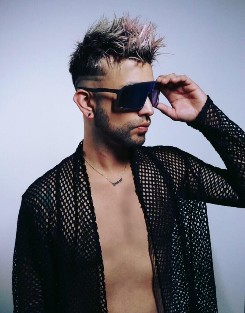 Jaime Adrian wearing a black mesh shirt with open buttons showing his chest, along with sunglasses.