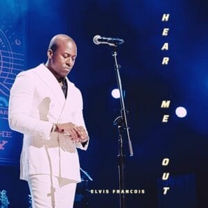 Promotional single cover artwork for "Hear Me Out" which shows Elvis Francois performing on stage in a white suit as the microphone stand is in front of him and blue LED lighting behind him.