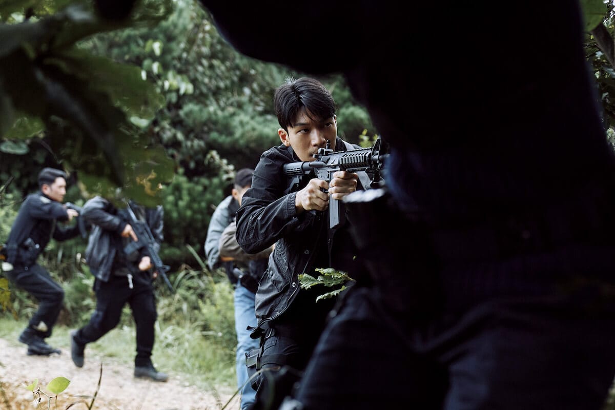 Squid Game Season 2 Shatters Netflix Records and Dominates Global Viewership 35 Still from Squid Game Season 2 which sees Wi Ha-joon playing Hwang Jun-ho, wearing black clothes and holding a gun in the middle of a wood land area.