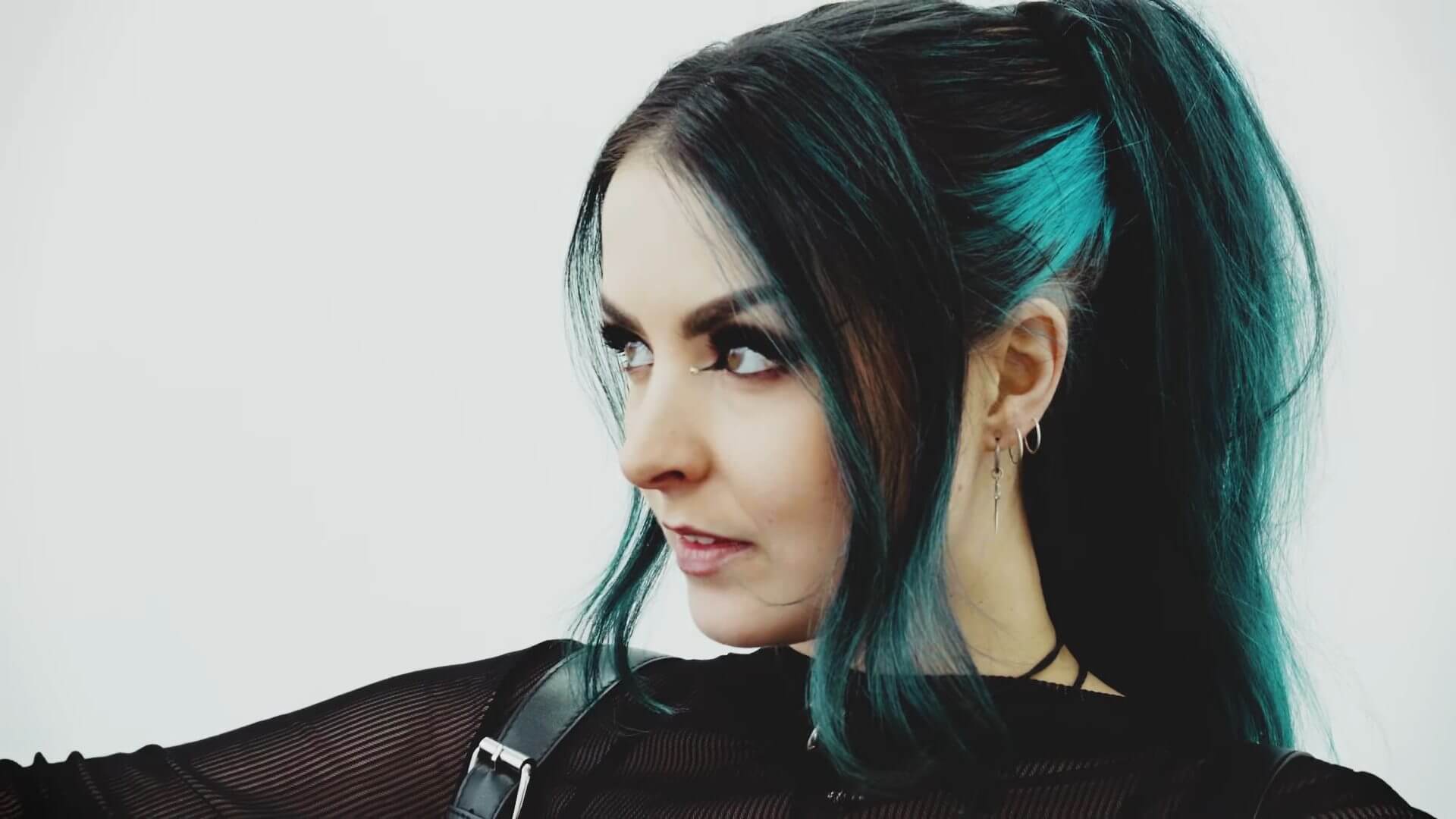 "Therapy": As December Falls Delivers a Hard-Hitting Anthem With Raw Relatable Energy and an Explosive New Music Video 19 Still from the "Therapy" music video which sees a close-up of frontwoman of As December Falls, Bethany Hunter, with her head turned to the side and her teal-blue hair pulled back into a ponytail.