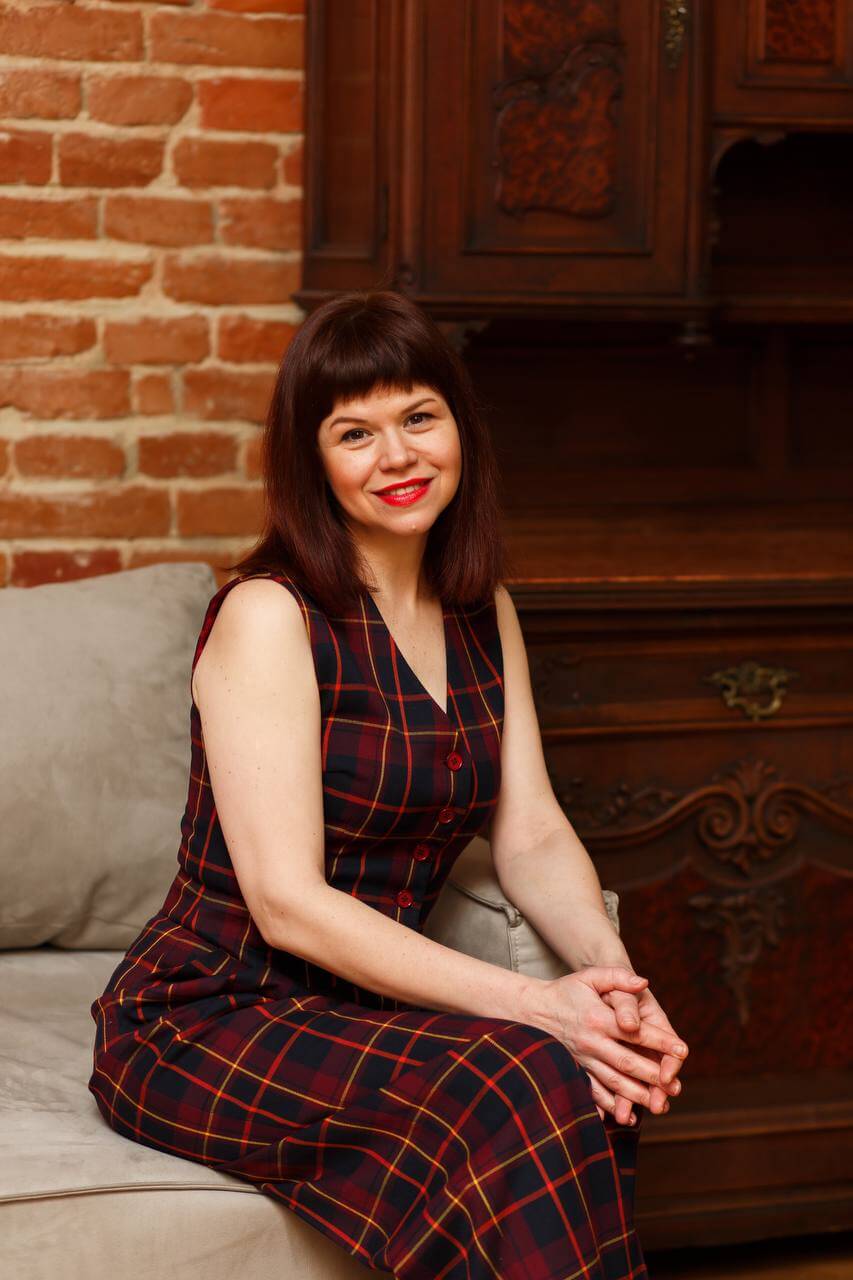 Ukrainian Writer Liudmyla Kalabukha's War-Time Business Guide "Do the Opposite" Has Been Nominated for the Prestigious Shevchenko Prize 2 Liudmyla Kalabukha posing on a grey couch, wearing a dark almost-black but navy dress with red chequered lines on it.