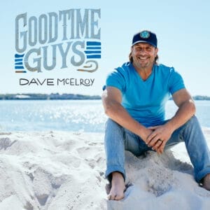 Official single cover artwork for "Good Time Guys" which sees Dave McElroy on a beach, with the sea behind him, wearing a dark blue trucker cap, a light blue t-shirt, and blue jeans. He's sitting on the sand, barefoot, while the song's title and his name are in blue ombre text in the upper-left.