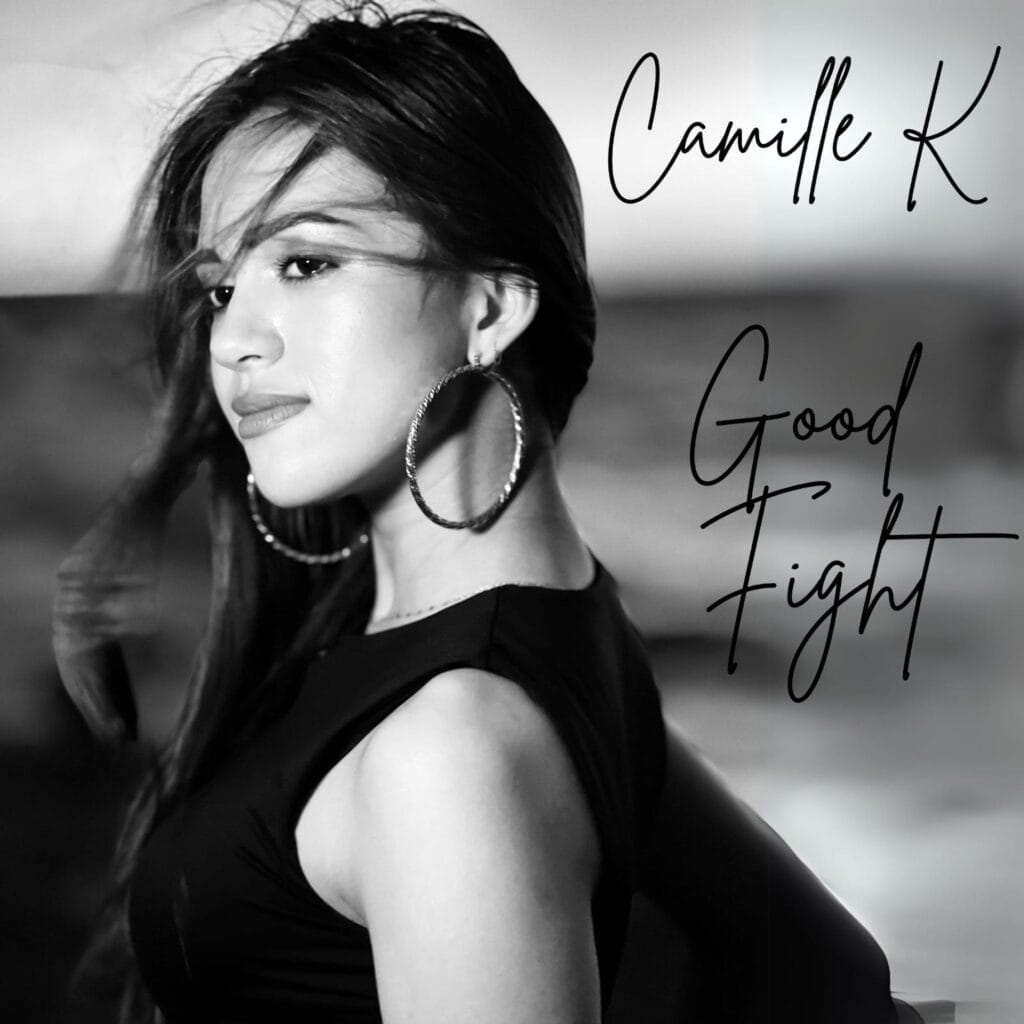 Official single cover artwork for "Good Fight" which is in black and white and sees Camille K looking at the camera with her body facing the left as the wind sweeps her hair over her right shoulder. The sea is blurred out in the background and her name and title are typed in cursive black writing on the right side of the image.