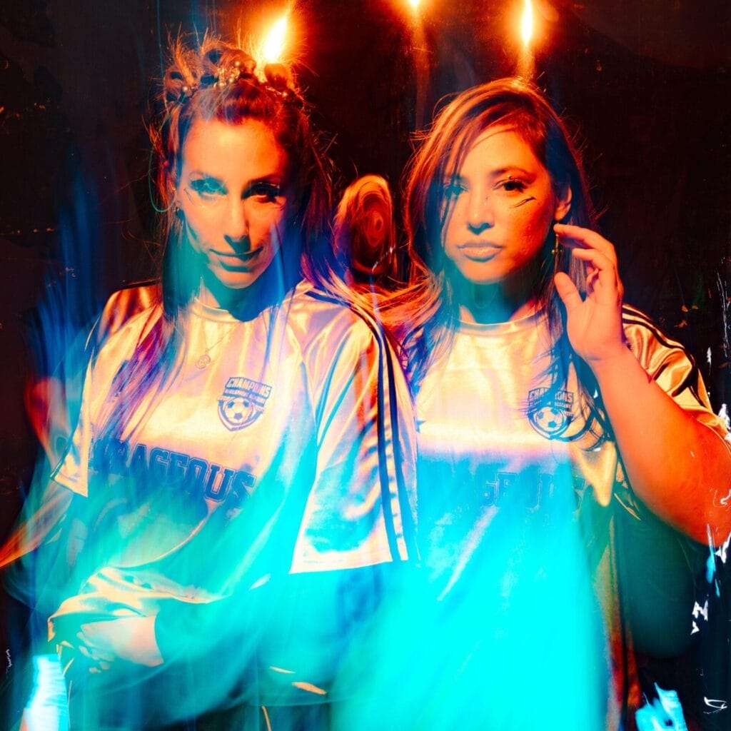 Official single cover artwork for "Fine On My Own" which sees the female duo Royal She posing for a photo while wearing what looks like football jerseys. There's a flame filter effect that can be seen in the foreground,, lighting up the image in blue.
