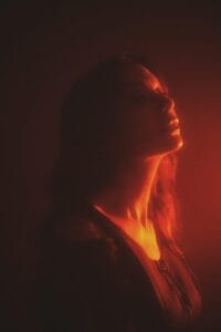 Promotional photo for "Paradise" which sees Marte Eberson looking up in wonder wearing a black top. The photo has a red haze filter to it.