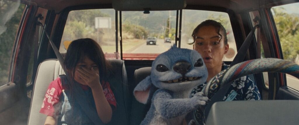 Stitch grabbing hold of the steering wheels as Nani acts surprised and Lilo laughs.