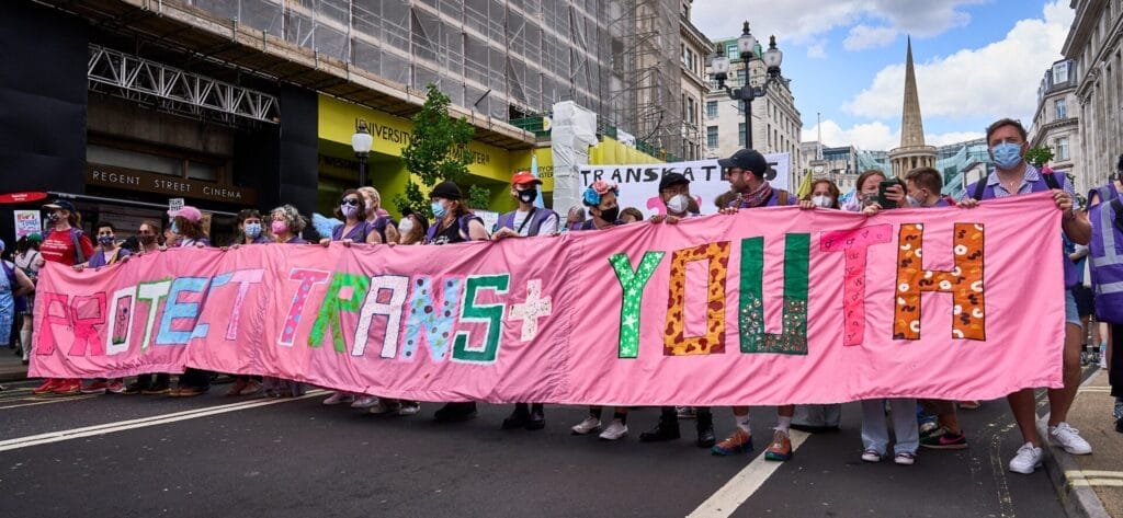 London Trans+ Pride 2025: Powerful Celebrity Messages Echo the Theme "Existence & Resistance" 117 Banner from London Trans+ Pride 2024 which says "Protect trans+ youth".