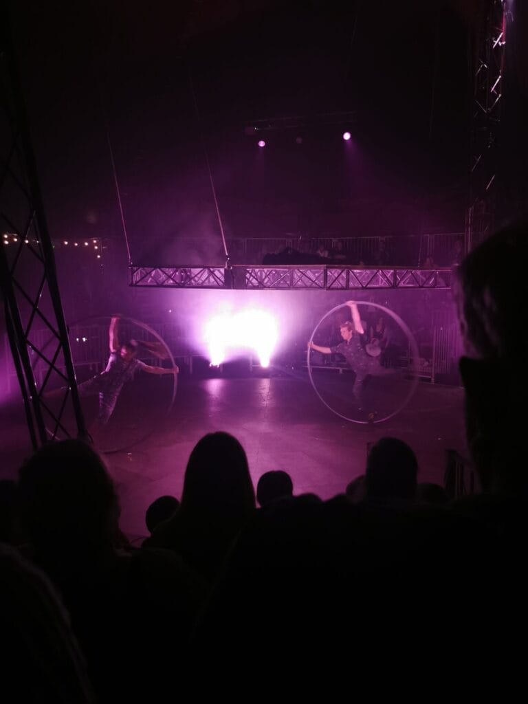 The Cyr Wheel duo performing their Cyr Wheel act together under the raised platform.