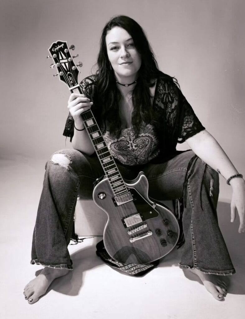 Lindsay Jordan Unveils Ethereal New Single “Trace the Moon” Ahead of Forthcoming EP 11 A black and white image of Lindsay Jordan sitting down with her guitar between her legs, wearing a black top and some ripped jeans.