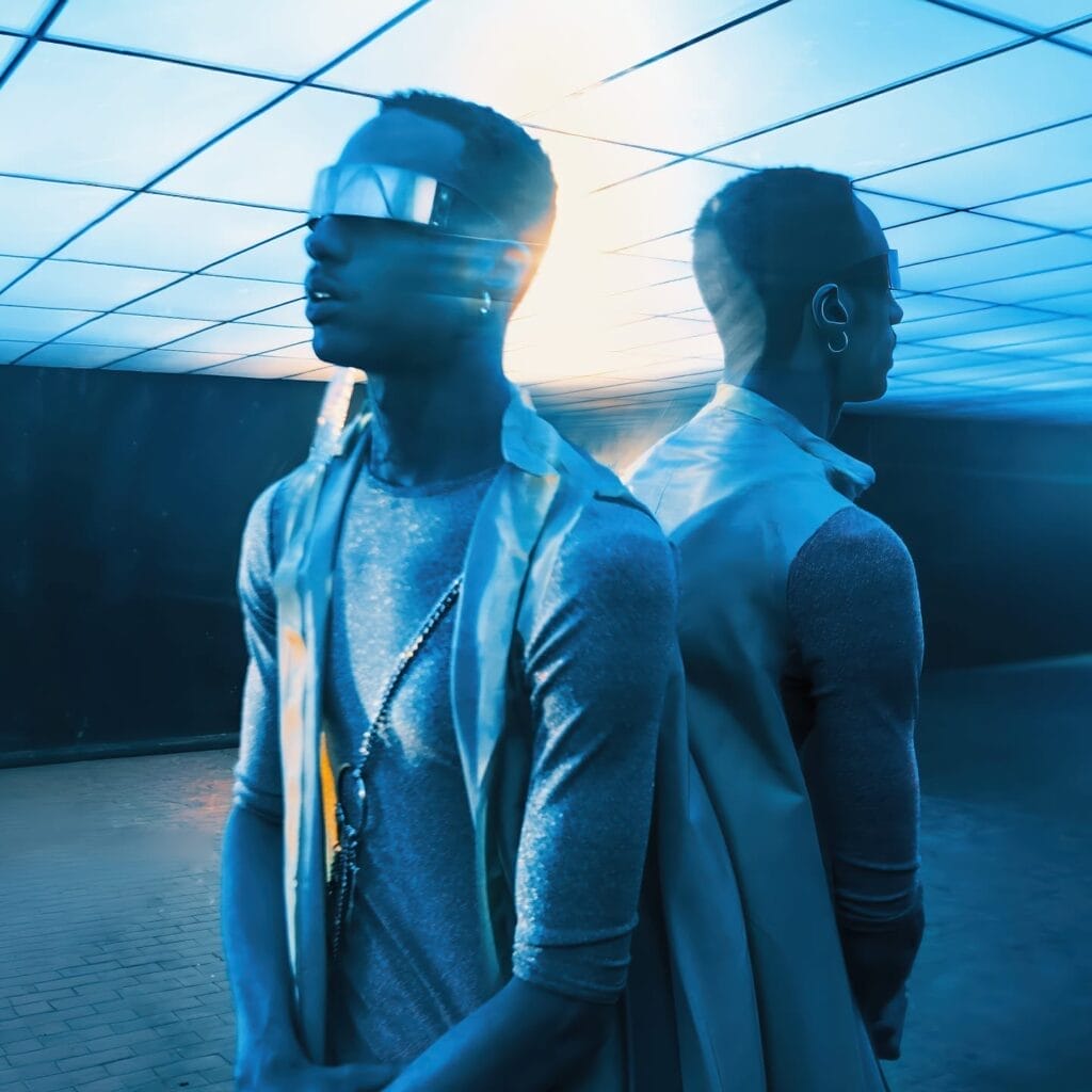 Exclusive Premiere: Aurelia & Icarus Moth Team Up with Ehiorobo on Mesmerising New Single and Visual Titled “SUPERNOVA” 4 Still from the "SUPERNOVA" music video which sees Ehiorobo leaning against a mirror, wearing a metallic outfit and a pair of shades whilst bathed in blue light.