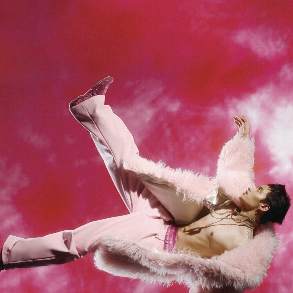 Official album cover artwork for "MAMA, I'M BACK" which sees BENZO falling through a pink sky of clouds. He has dark hair and is shirtless while wearing a fluffy pink jacket and pink trousers.